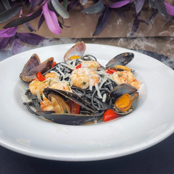 Squid ink pasta with mussels, shrimp, red peppers, and grated cheese on a white plate.