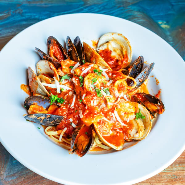 Linguine pasta with mussels, clams, and shrimp in a rich red sauce, garnished with parsley and cheese.