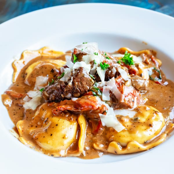 Close-up of ravioli with a rich brown sauce, topped with shredded meat, tomatoes, and parmesan cheese.