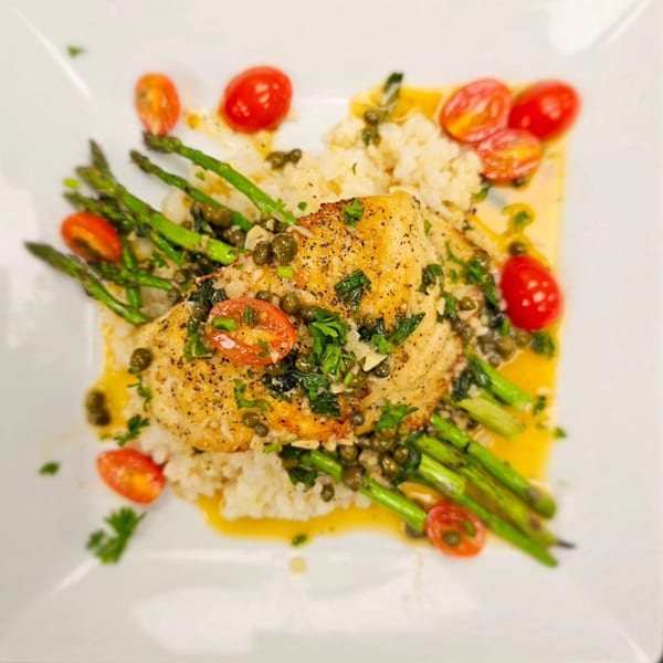 Pan-seared fish with capers, cherry tomatoes, asparagus, and rice, drizzled with sauce.