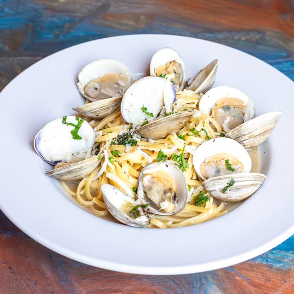 Linguine pasta with clams, parsley, and grated cheese in a white bowl.