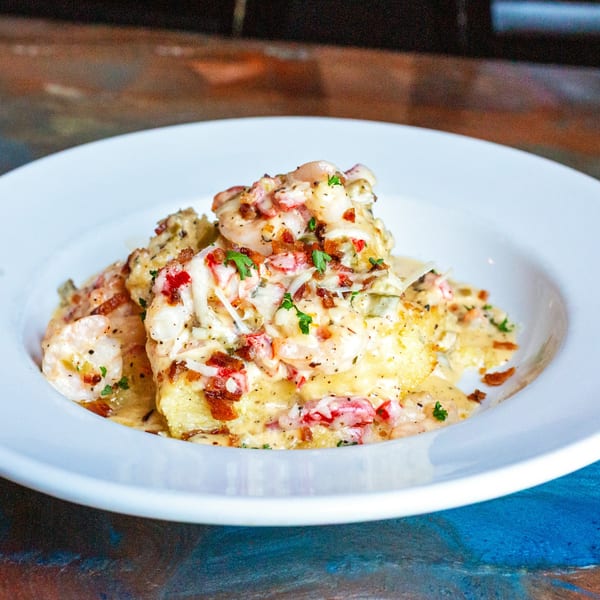 Creamy shrimp and grits topped with bacon bits and parsley in a white bowl.