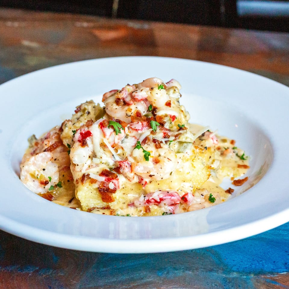 Creamy shrimp and grits topped with bacon bits and parsley in a white bowl.