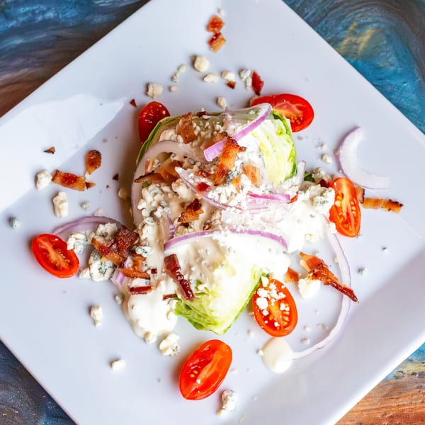 Wedge salad with blue cheese dressing, bacon, red onion, and cherry tomatoes on a white plate.
