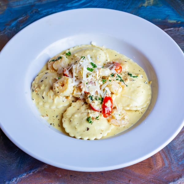 Shrimp ravioli in a creamy sauce, topped with shredded cheese, parsley, and cherry tomatoes.