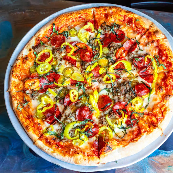 A whole pizza with pepperoni, sausage, banana peppers, and basil on a metal tray.